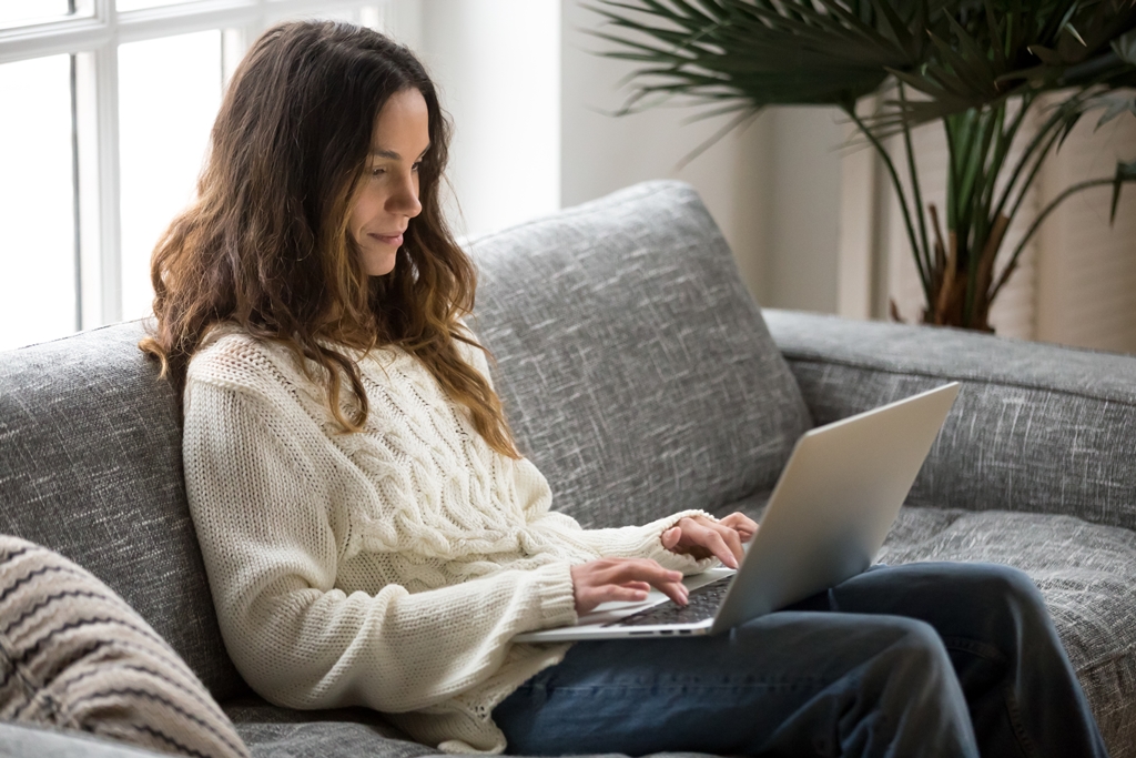 Woman working on a laptop while sitting comfortably on a couch.