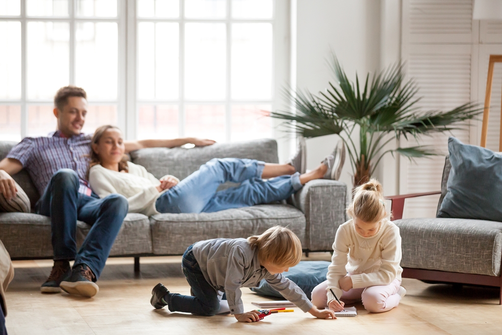 A family relaxing in a living room with two children colouring on the floor and parents sitting on the couch.