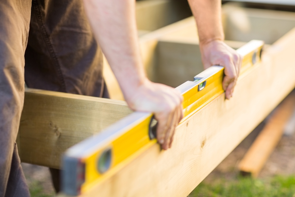 A person using a spirit level to check the horizontal alignment of a wooden beam.