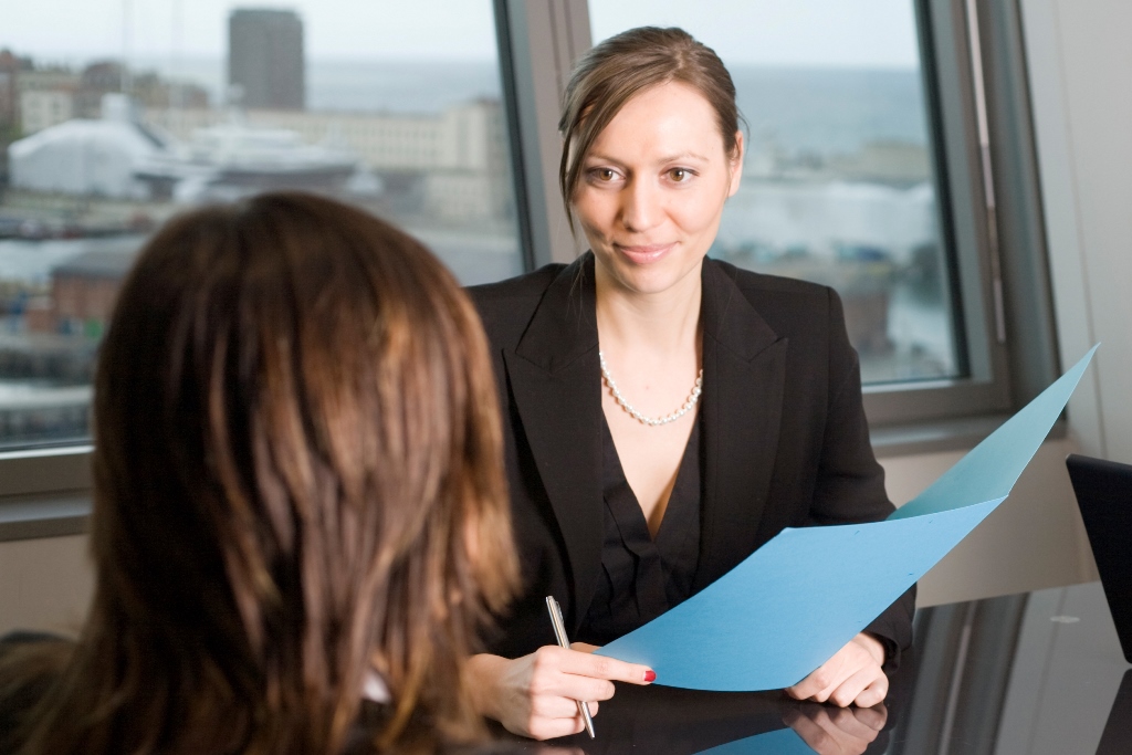 A professional woman holding a document during a meeting with another individual across the table.