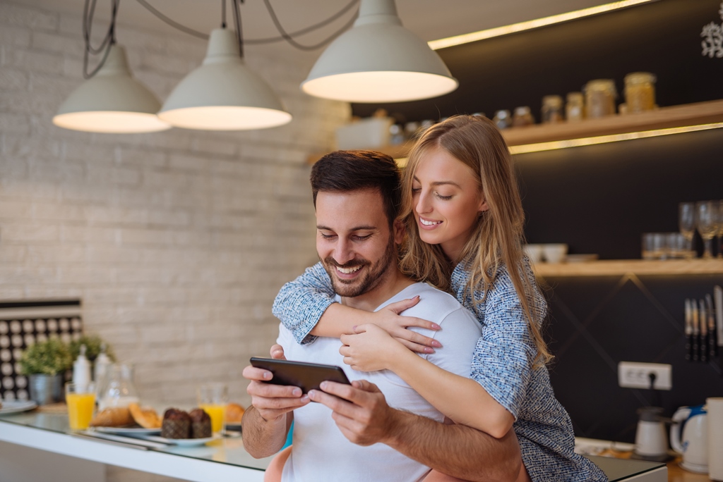 A couple smiling and looking at a smartphone together in a modern kitchen.