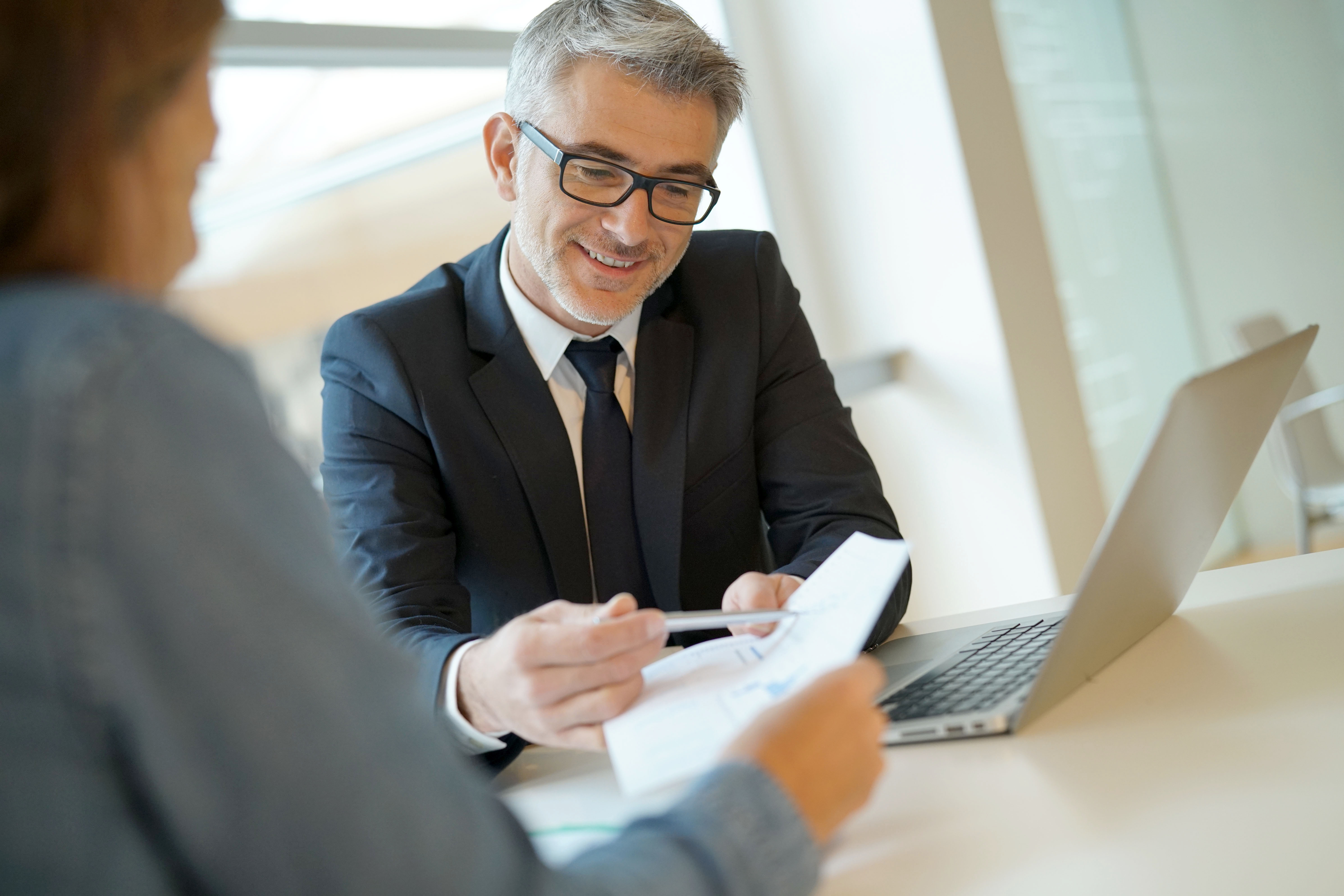 Business professional in a suit reviewing documents with a colleague at a workplace.